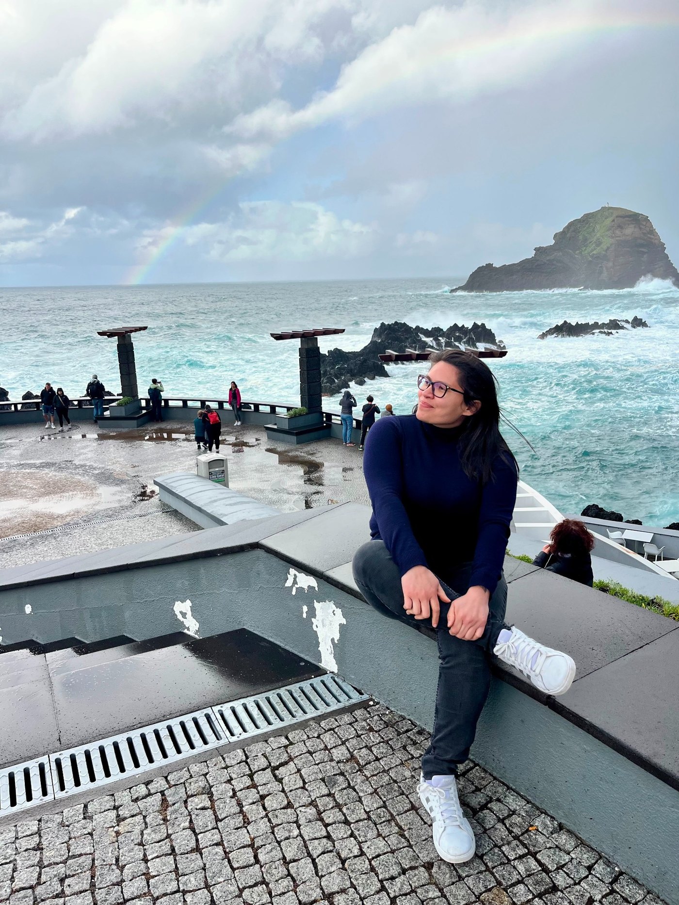 Iara Teixeira in Madeira, Portugal, with the Atlantic Ocean and rainbow in the background.